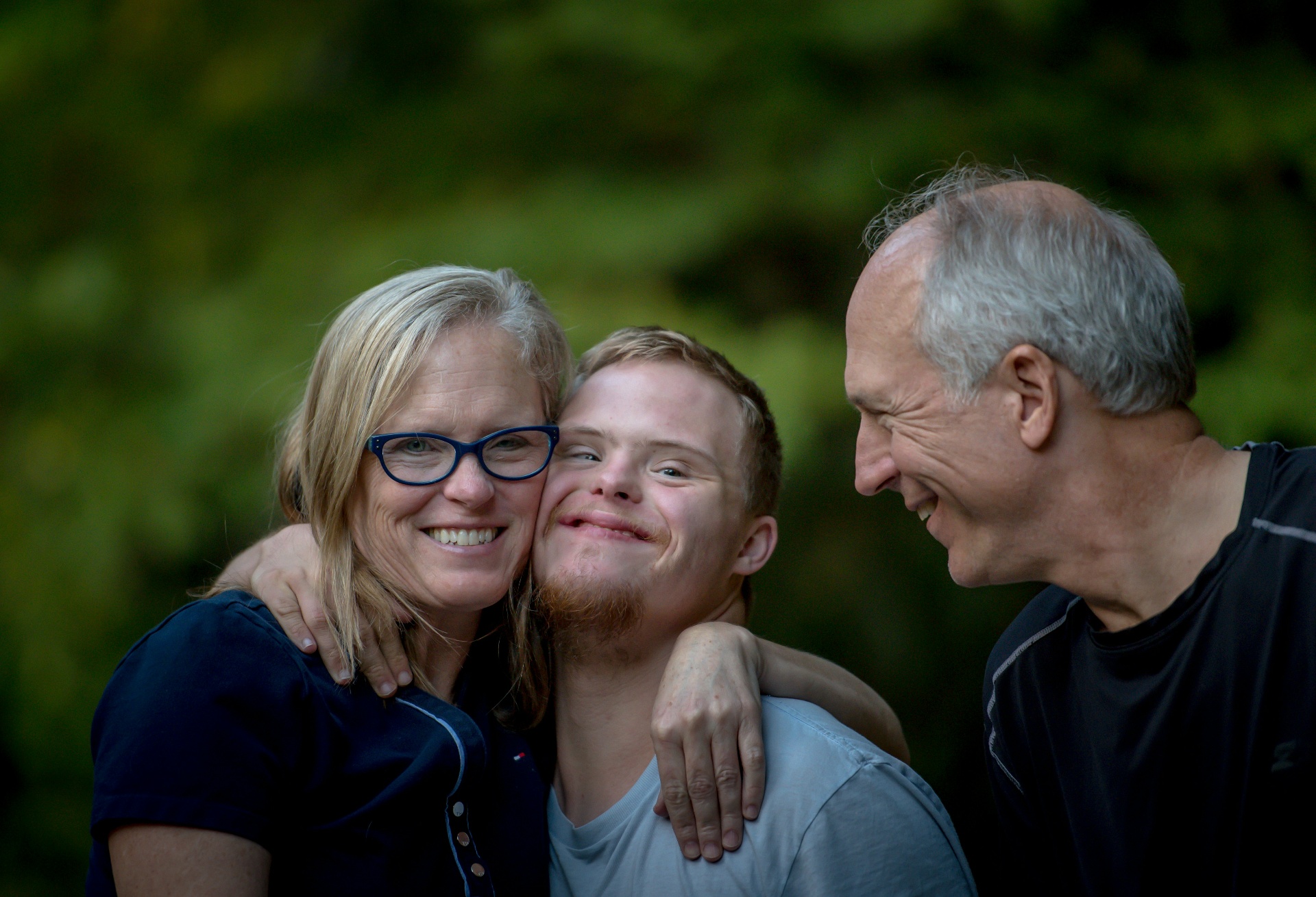 A mother, son, and father sharing a warm embrace outdoors