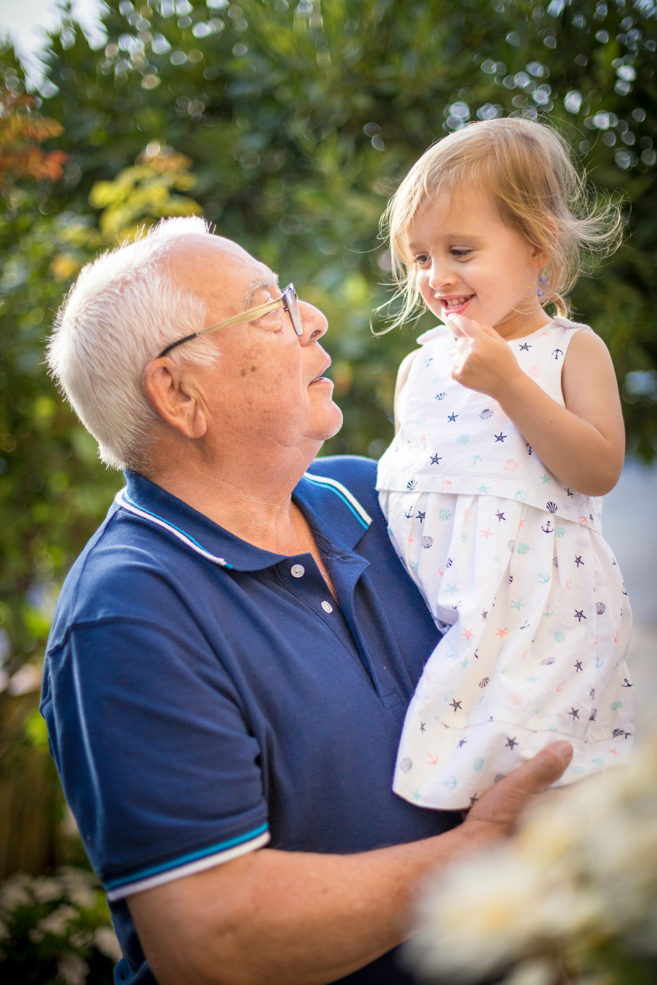 A grandfather holding his young granddaughter outdoors, a moment of protection across generations