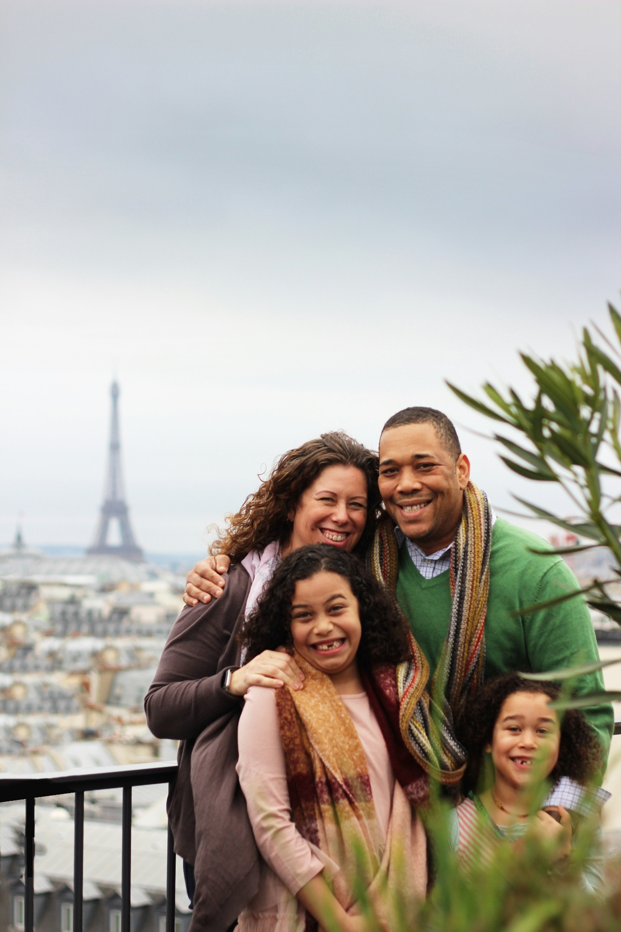 A family of four smiling together on a Paris rooftop with the Eiffel Tower in the distance